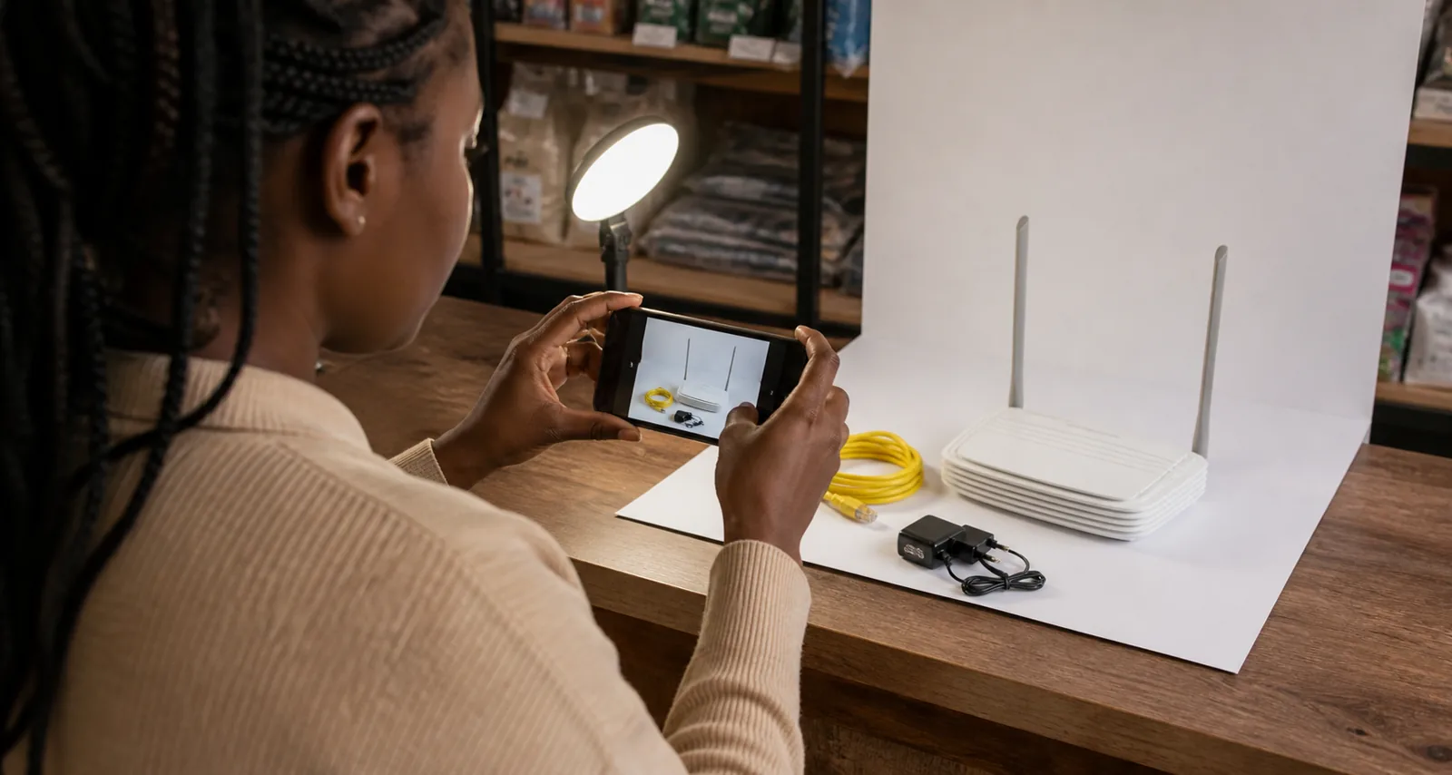 Kenyan seller photographing an electronic product beside a window with a plain background